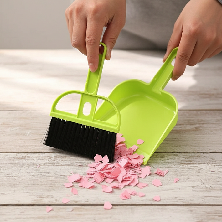 balayette pelle verte qui ramasse  des miettes du papier rose